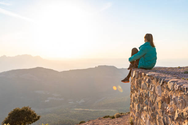 istock Beautiful woman sitting on an edge during sunset with mountains 1438665456