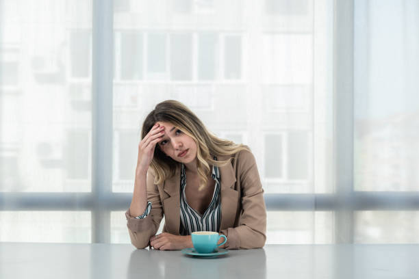 But first coffee. Young unhappy tired business woman in formal wear sitting in the office at empty desk with cup of coffee. Female white collar worker, freelancer financial expert morning routine. But first coffee. Young unhappy tired business woman in formal wear sitting in the office at empty desk with cup of coffee. Female white collar worker, freelancer financial expert morning routine. bad coffee stock pictures, royalty-free photos & images