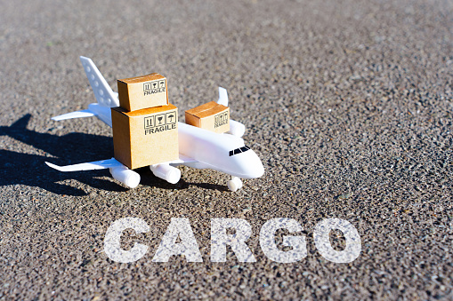 Word CARGO written on the runway in front of a toy aircraft carrying tiny shipping boxes.