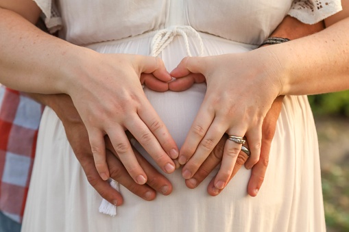 The married couple forming a heart shape with hands on the pregnant belly of the woman
