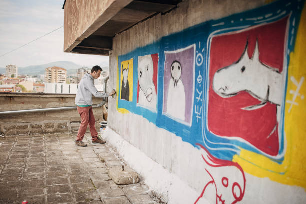 One male, male artist painting a graffiti on the wall on building top.