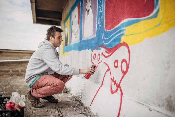 One male, male artist painting a graffiti on the wall on building top.