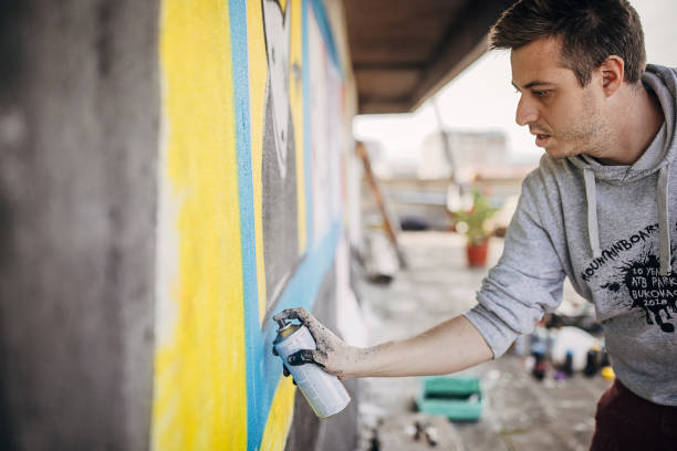 One male, male artist painting a graffiti on the wall on building top.