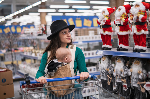 Young woman carrying her baby and shopping for Christmas decoration.