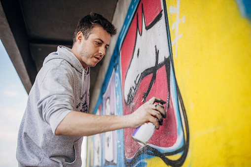 One male, male artist painting a graffiti on the wall on building top.