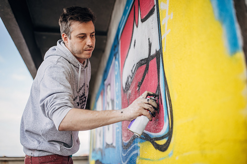 One male, male artist painting a graffiti on the wall on building top.