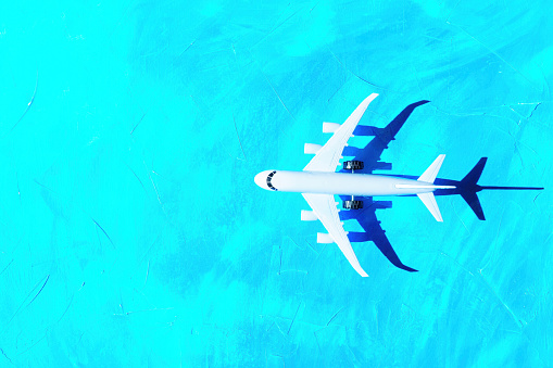 Toy airplane model flying over a turquoise background imitating the ocean. Air transport related concept.