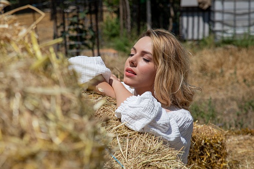 blonde woman in a white dress crossing her arms on a haystack square