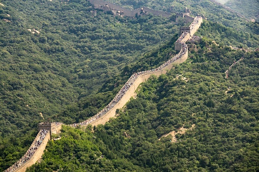 A high angle shot of the famous Great Wall of China surrounded by green trees in summer