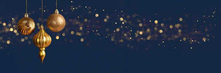 Christmas banner with three golden balls decorations on blue background with bokeh lights with copy space. Wide panoramic header