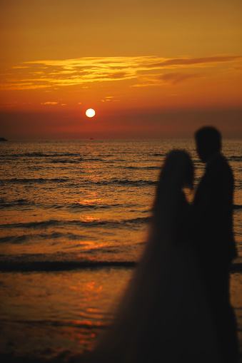 Silhouette of newlyweds bride and groom are hugging on sunset or sunrise on beach. Loving couple by the sea. Ocean romantic ceremony. Wedding day. February 14, St. Valentine's Day. honeymoon.