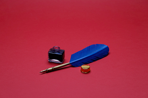 inkwell with blue feather on the red background