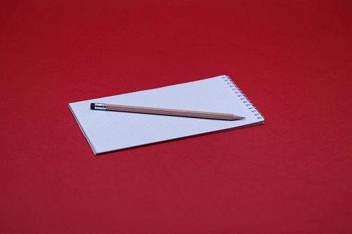 notepad with wooden pencil on the red background