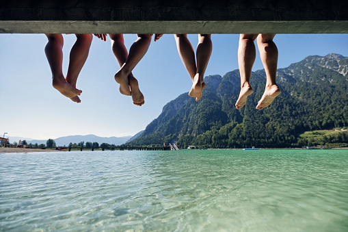 Mother and teenage kids enjoying summer vacations. They are sitting on pier on a lake Achensee in Austrian mountains. 
Sunny summer day.
Canon R5