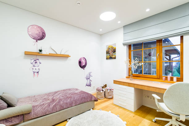 Bright coloured child room. Single bed and work table by the window. Wall decorated with drawings.