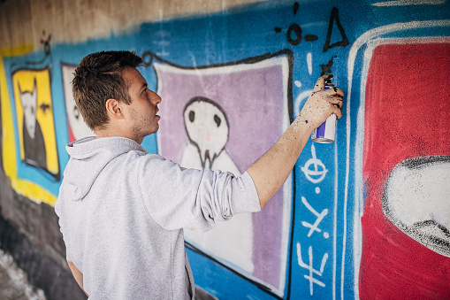 One male, male artist painting a graffiti on the wall outdoors.