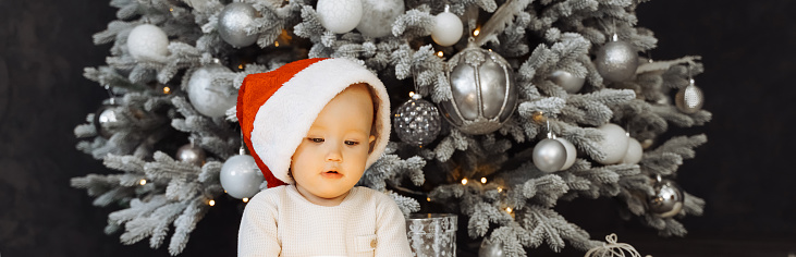 Handsome toddler cute in Santa hat smile happily over defocused Christmas background