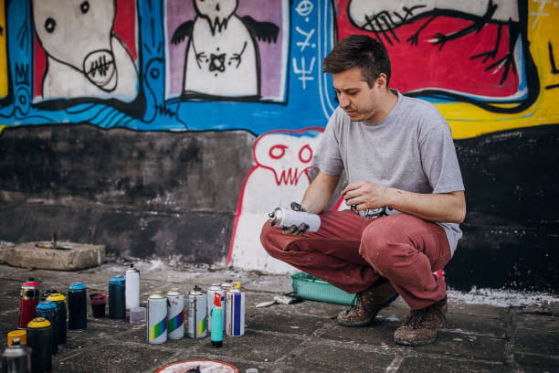 One male, male artist standing by the graffiti that he painted on the wall on building.