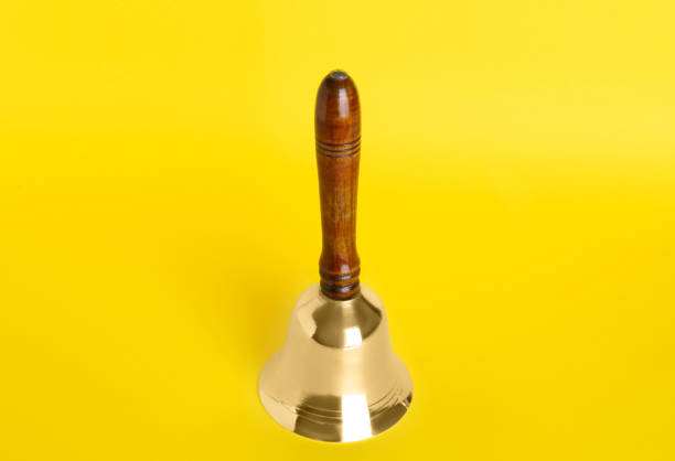 istock Golden school bell with wooden handle on yellow background 1438690832