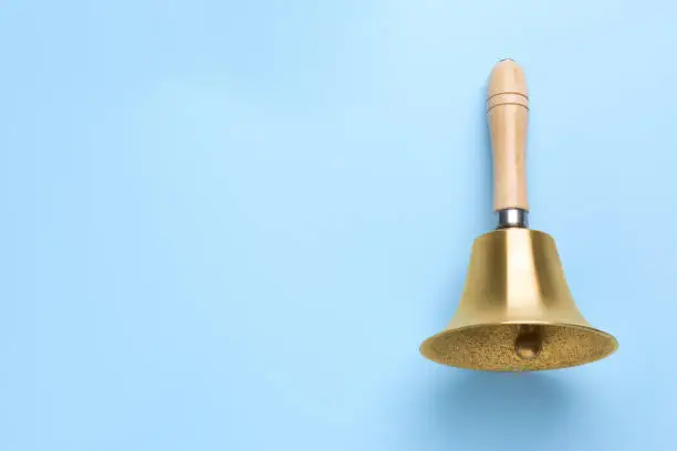 Golden school bell with wooden handle on light blue background, top view. Space for text