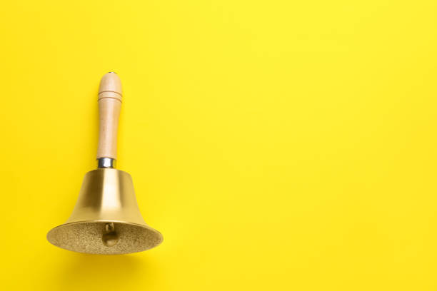 istock Golden school bell with wooden handle on yellow background, top view. Space for text 1438691332