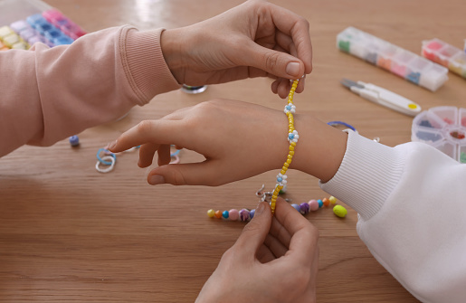 Mother with her daughter making beaded jewelry at table, closeup