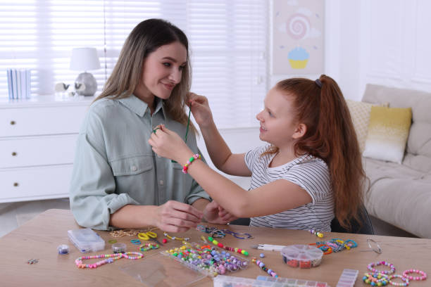 happy mother with her daughter making beaded jewelry at home - necklace jewelry bead homemade imagens e fotografias de stock