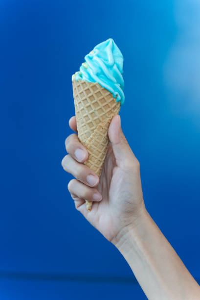 istock Female hand holding blue ice cream cone on blue background. 1438691915