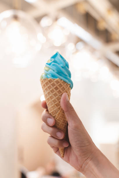 istock Female hand holding blue soft serve ice cream with blurred background. 1438691920