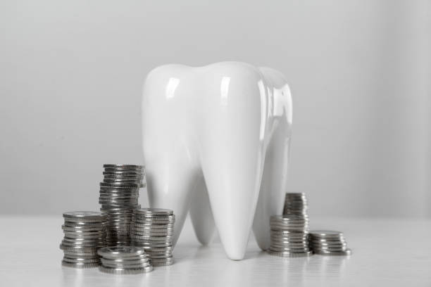 istock Ceramic model of tooth and coins on white table. Expensive treatment 1438691961