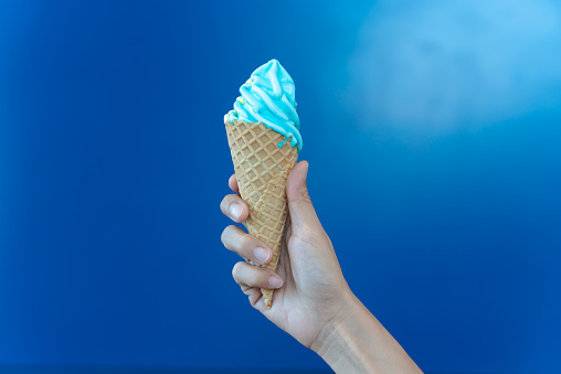 Woman hand holding a cone of blue soft serve ice cream on blue background.