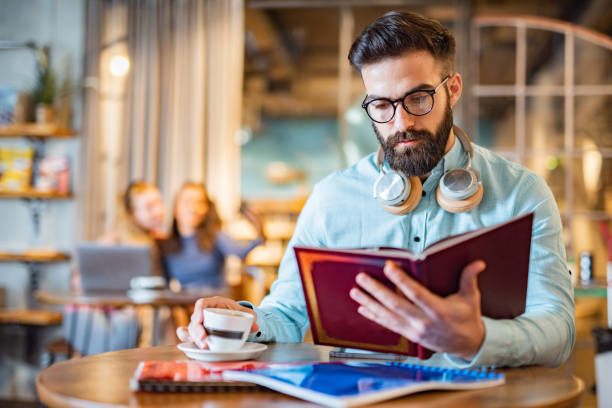 istock Man reading a book in university cafe 1438693350