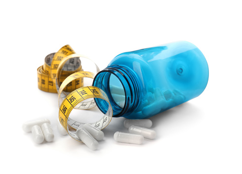 Jar of weight loss pills and measuring tape on white background