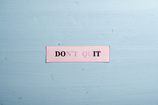 Dont quit sign vanishing into a do it sign written on a pale pink paper placed over blue background
