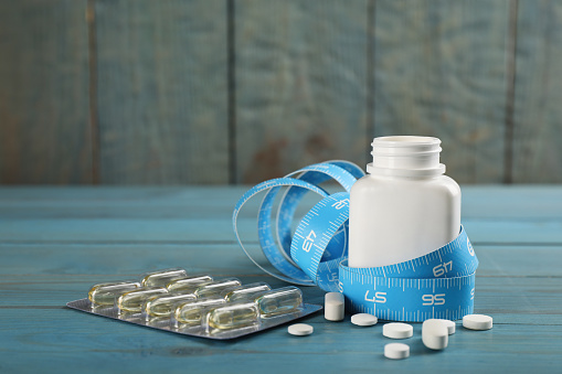 Weight loss pills and measuring tape on light blue wooden table. Space for text