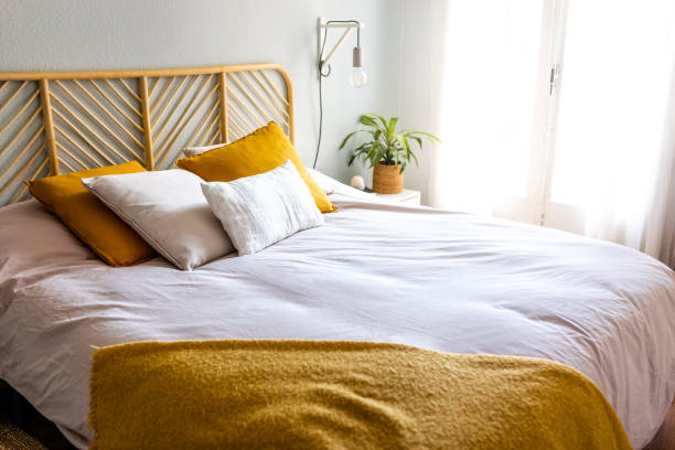ベッド、ランプ、クッション、植物を備えた明るく風通しの良い居心地の良いベッドルーム。人はいません。家のインテリア