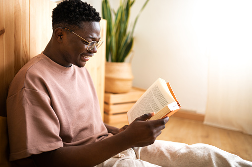 Relaxed African American young man reading a book at home. Copy space. Lifestyle.