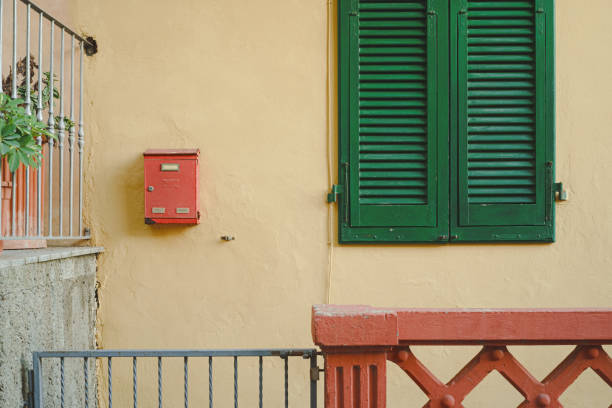 Colorful corner of an Italian house: green window, red mailbox and fence, yellow wall.