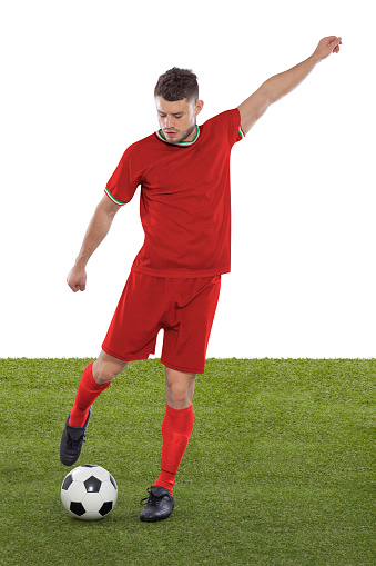 Professional soccer player with red IR IRAN national team jersey about to score a goal with an expression of challenge and decision on his face on white background.