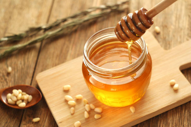 flower honey Honey is in a jar on a wooden table. Honey flows down the honey stick into the jar. Nearby are pine nuts and rosemary. selective focus honey stock pictures, royalty-free photos & images