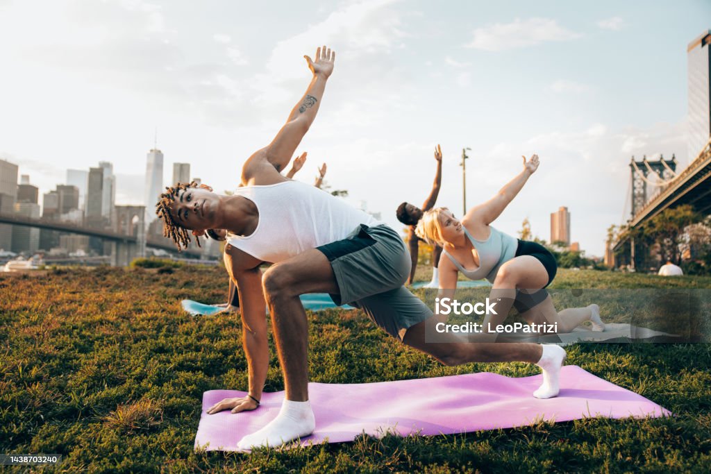 Yoga outdoor class in New York Group of young people attending to a yoga class outdoors at sunset with New York cityscape on their background. They are meditating and relaxing. Yoga Stock Photo