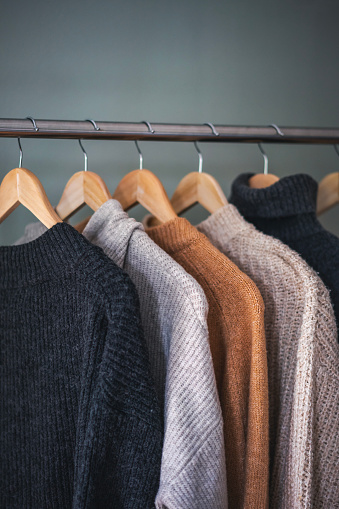 Warm cozy sweaters in neutral gray and beige shades hanging on hangers
