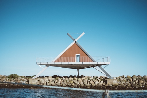 A shot of a triangle-shaped house in front of water under a blue sky