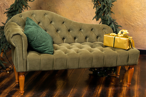Christmas composition with decoration, christmas tree branch, stylish green classic sofa, gift boxes and accessories in cozy home decor. Happy xmas and New Year holiday concept. Vertical photo.