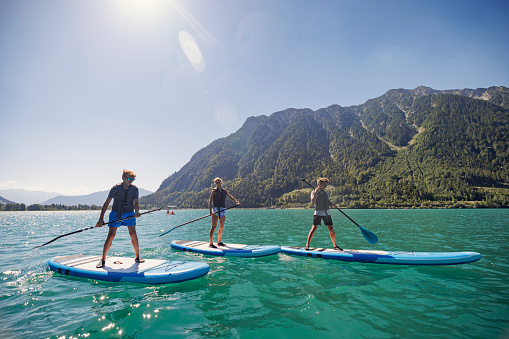 Teenagers enjoying summer vacations. They are enjoying SUP paddleboards on Achensee lake in mountains of Tyrol, Austria.\nCanon R5