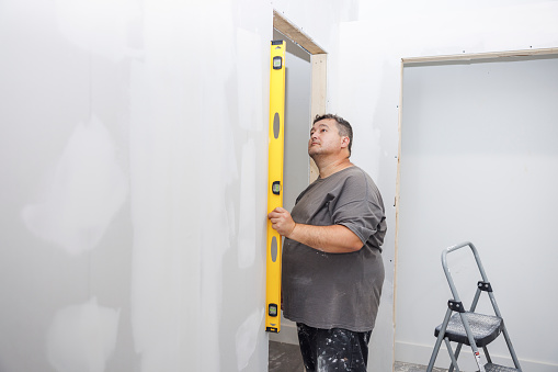 Leveling the wall in the new house. Caucasian repairman measuring the wall with a building level.