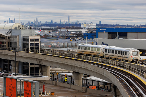 New York City, USA - April 8, 2022: JFK International Airport, one of the busiest in the world, is active even in stormy weather in early morning. Airtrain is going to the terminal 7. Manhattan skyscrapers are visible behind.