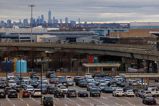 New York City, USA - April 8, 2022: JFK International Airport, one of the busiest in the world. Blue Parking in Terminal 4 with cars and Manhattan skyline with Freedom Tower in the early, cloudy morning behind.