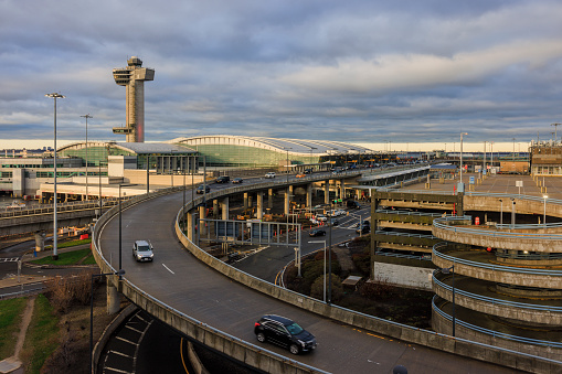 New York City, USA - April 8, 2022: JFK International Airport, one of the busiest in the world, is active even in stormy weather in early morning. Multilevel parking in Terminal 4 with Control Tower behind. Expressway with the traffic on it at the front.