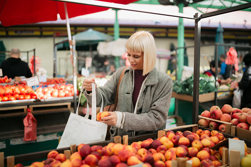 Happy woman with blond hair browsing through fruits at the farmer's market, picking up some peaches for herself